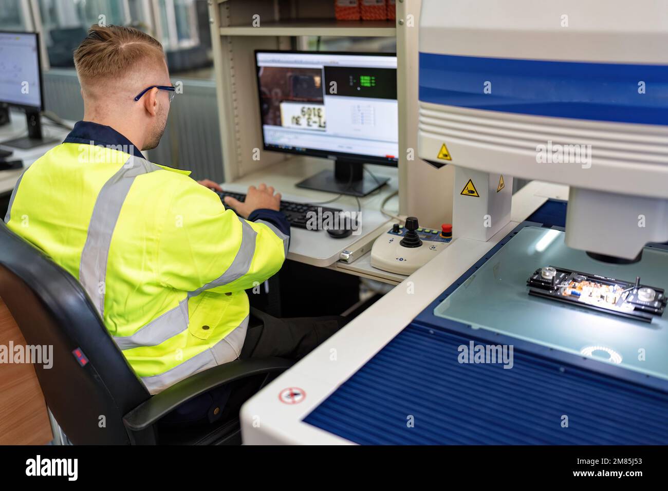 Techniker, der im Roboterherstellungsraum sitzt, verwenden das Messmikroskop, um die elektronische Platine zu prüfen Stockfoto