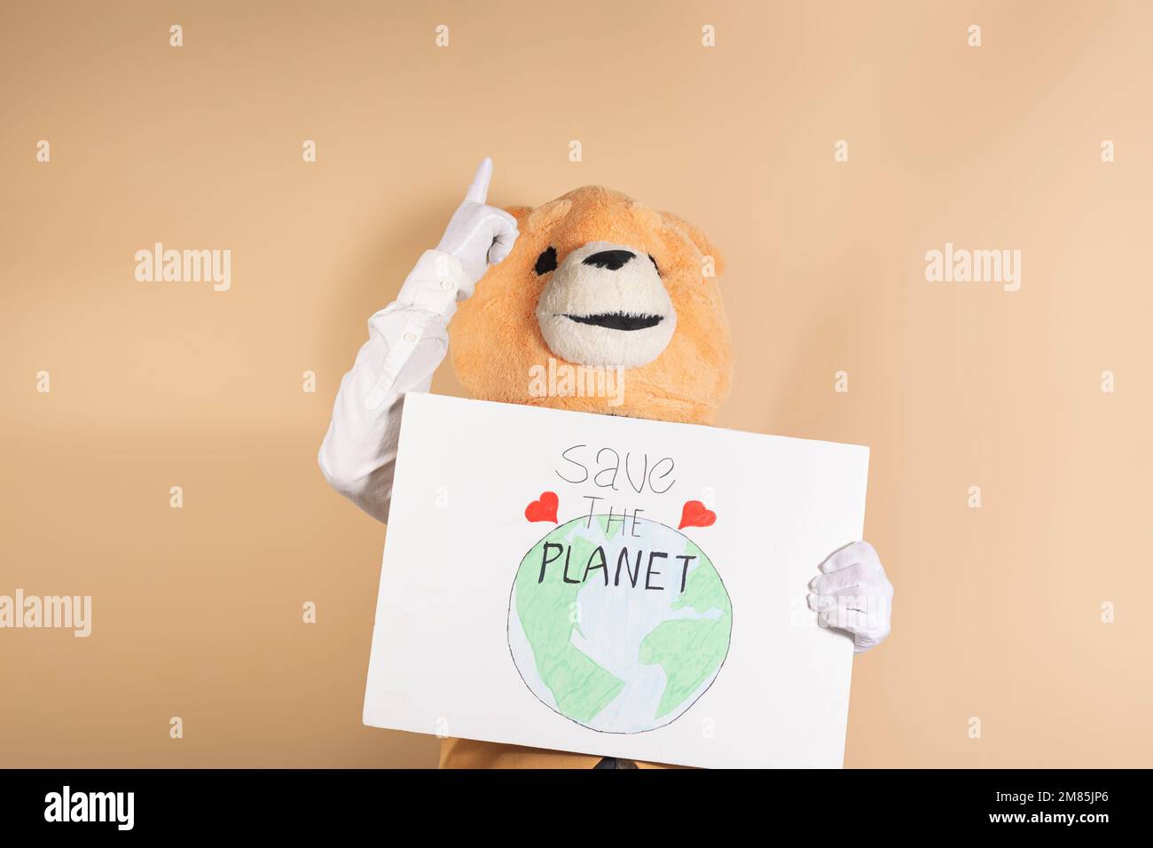 Ein Mann mit einer Teddybärmaske auf gelbem Hintergrund zeigt nach oben und hält ein Pappschild mit der Aufschrift "Rettet den Planeten". Stockfoto