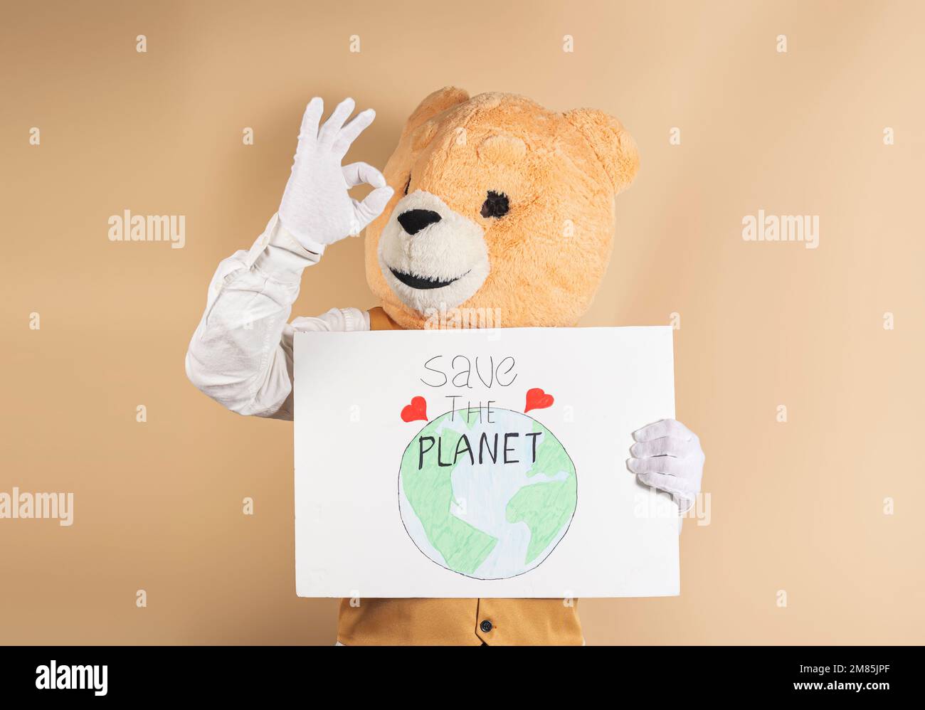 Teddybär mit einem menschlichen Körper, der OK zeigt, während er ein Schild mit der Aufschrift „Rettet den Planeten“ hält. Stockfoto