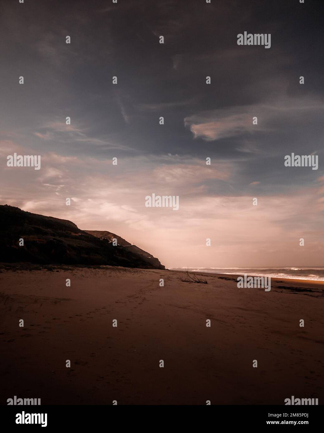 Traumhafte Landschaft mit leerem Strand bei Sonnenaufgang mit einem langen Sandstrand und felsiger Küste in der Ferne. Atmosphärische Stimmung mit vertikaler Ausrichtung Stockfoto