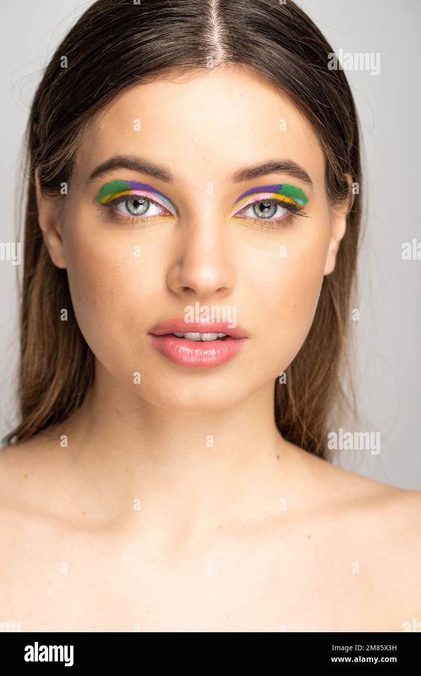 Brünette Teenagerin mit kreativem Make-up, die auf grau isoliert in die Kamera schaut Stockfoto