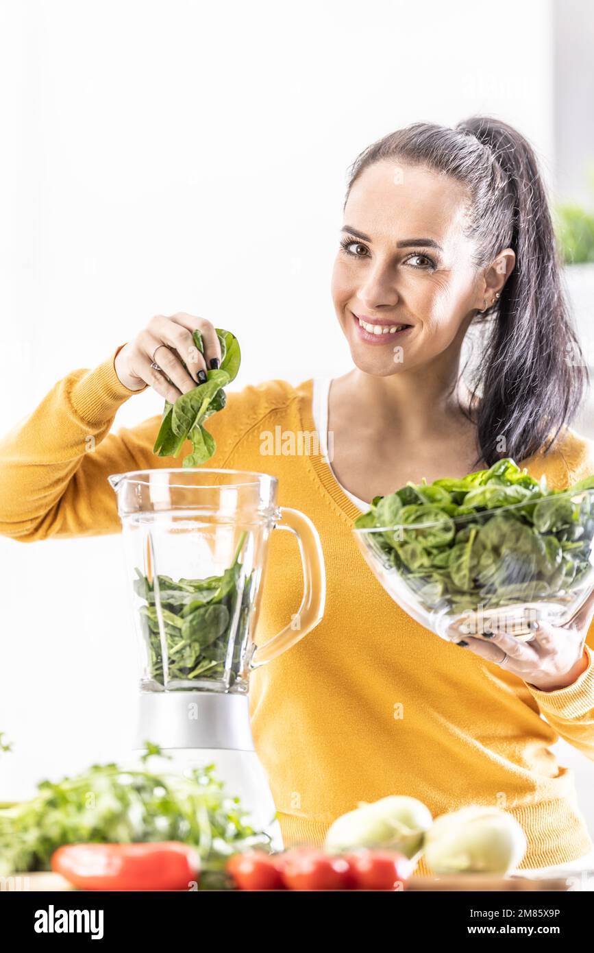 Lächelnde Frau, die Spinat-Smoothie macht, Blätter in den Mixer gibt. Konzept einer gesunden Lebensweise und Ernährung. Stockfoto