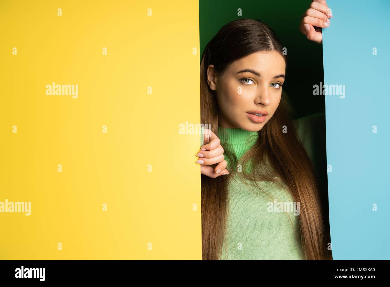 Brünette Teenagerin posiert und schaut auf die Kamera vor farbenfrohem Hintergrund Stockfoto