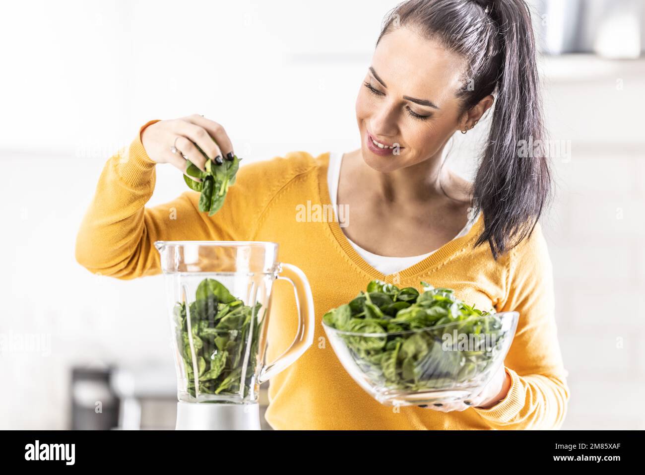 Lächelnde Frau, die Spinat-Smoothie macht, Blätter in den Mixer gibt. Stockfoto
