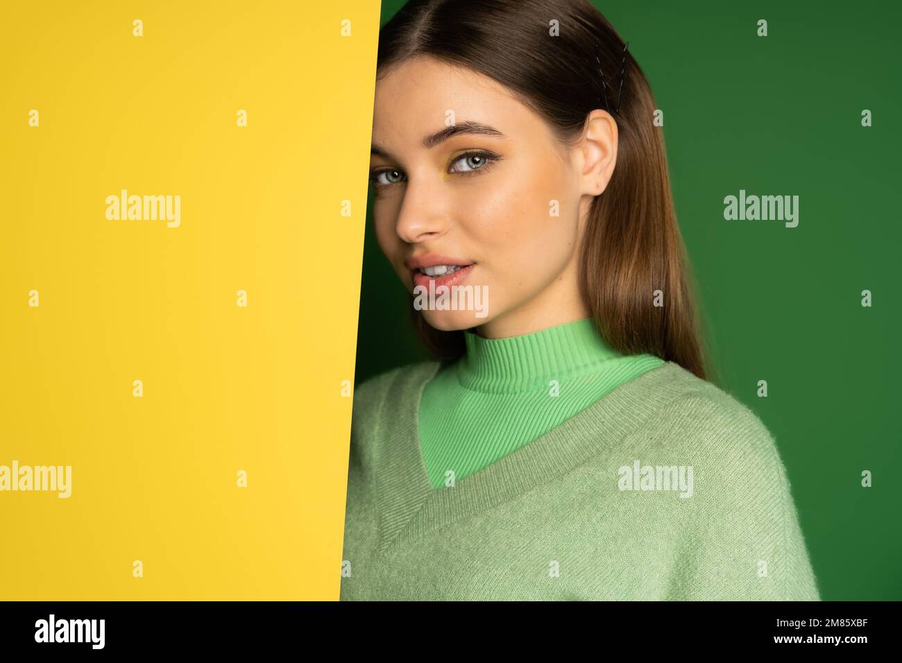 Braunes Teenager-Mädchen im Pullover, das vor der Kamera lächelt, auf farbenfrohem Hintergrund Stockfoto