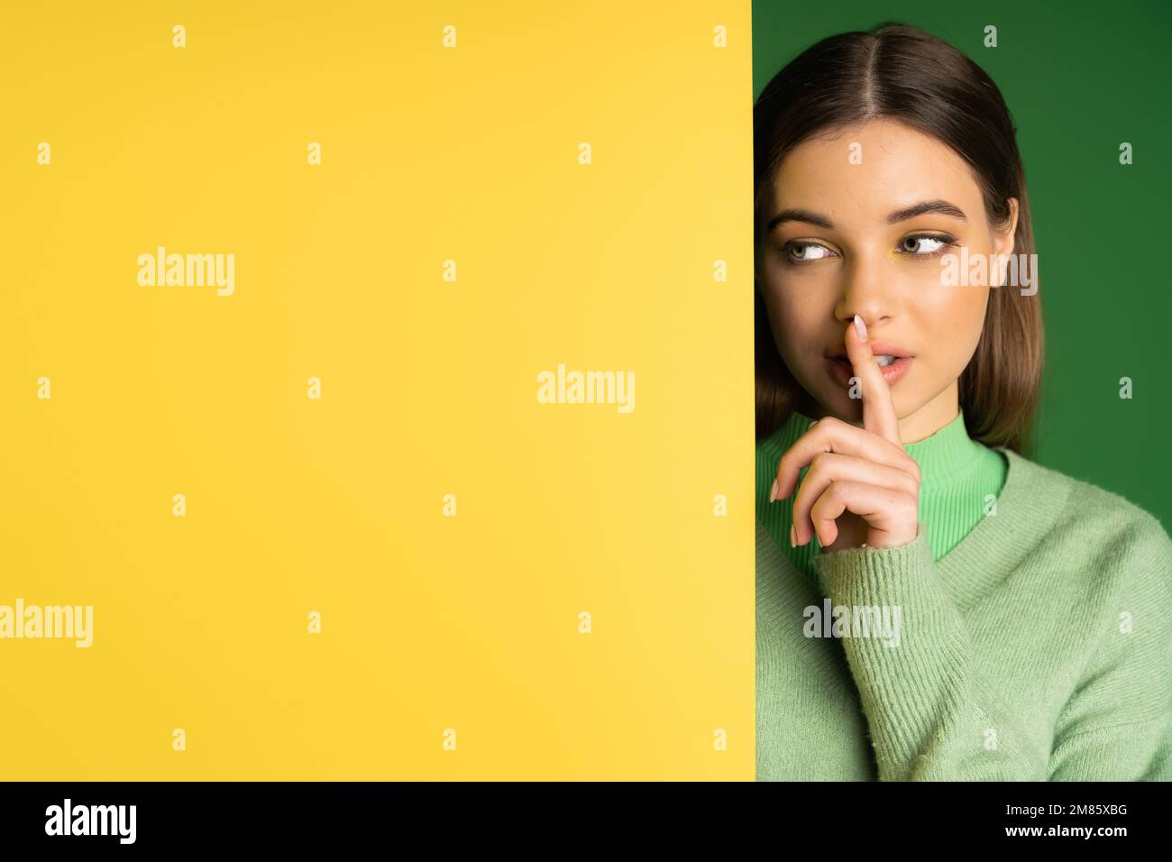 Braunes Teenager-Mädchen, das ein Sh-Schild neben gelbem und grünem Hintergrund zeigt Stockfoto