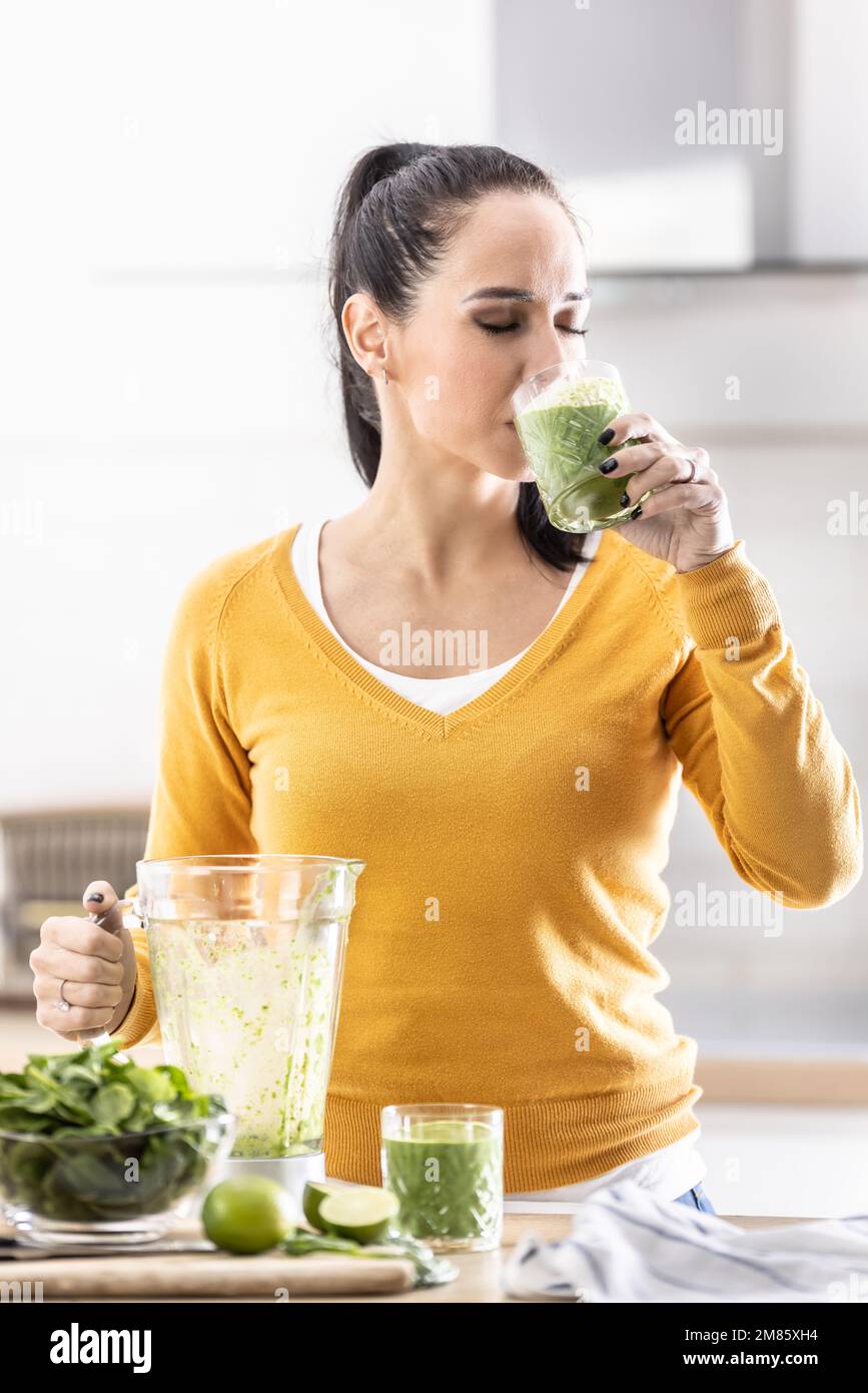 Eine junge Frau mag einen Spinat-Smoothie, den sie selbst gemacht hat. Sie trinkt ein Gemüse-Energydrink. Stockfoto