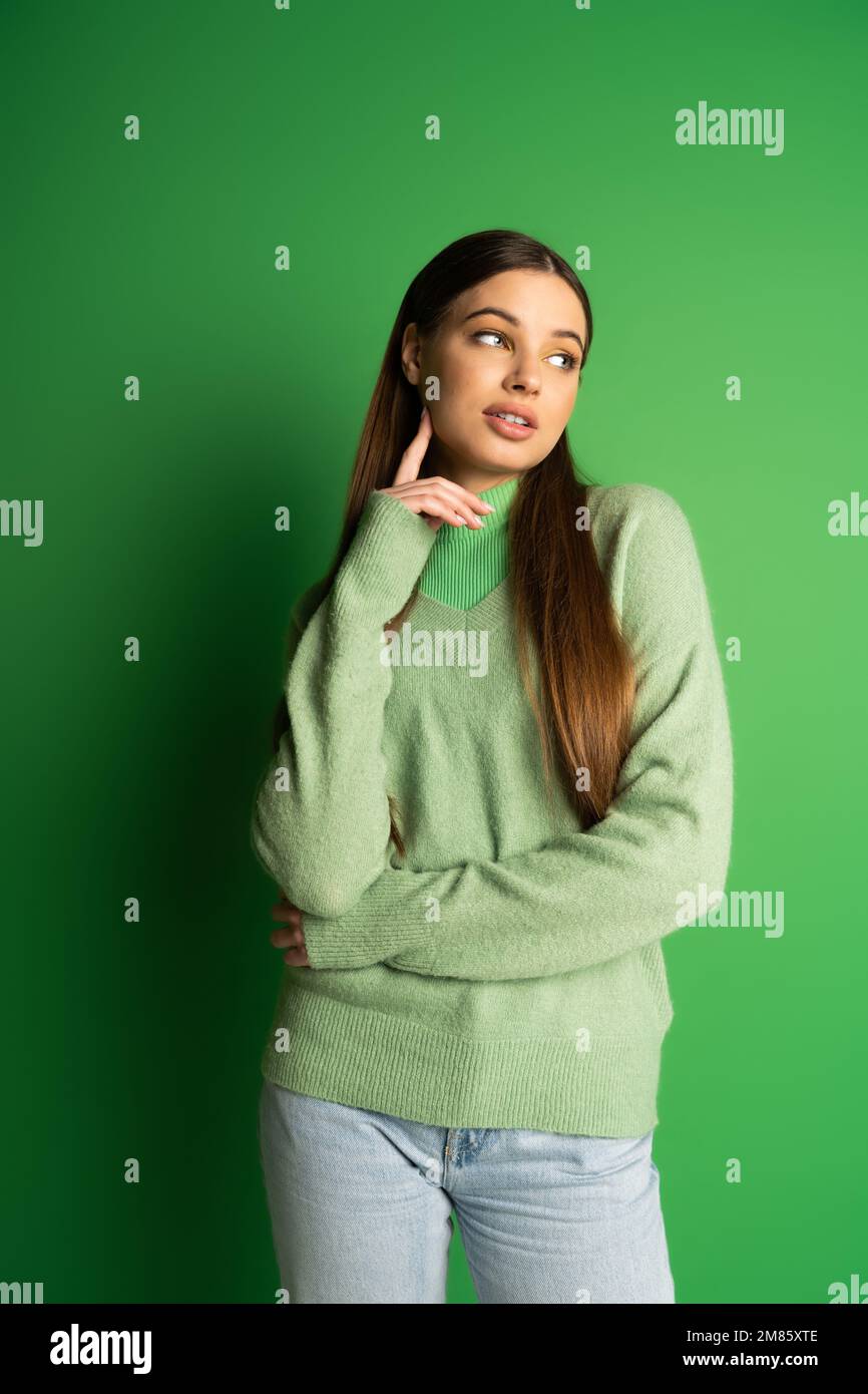 Brünette Teenagerin im Pullover, die auf grünen Hintergrund wegschaut Stockfoto