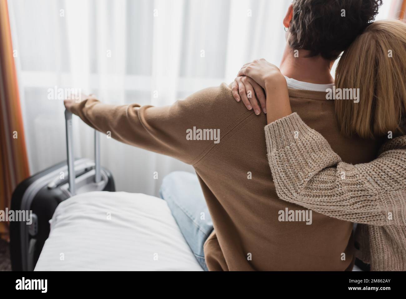 Rückansicht einer blonden Frau, die ihren Freund umarmt, während sie im Hotel auf dem Bett sitzt, Stockbild Stockfoto