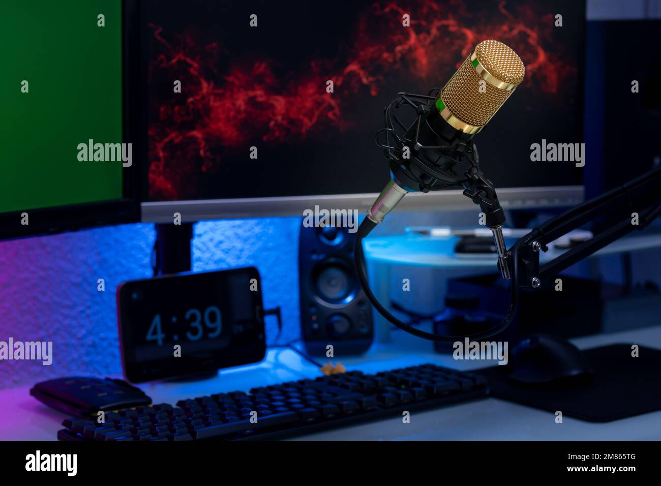 Kondensatormikrofon im Gamer-Setup mit Monitoren, Tastatur, Maus und farbigen Lichtern. Stockfoto