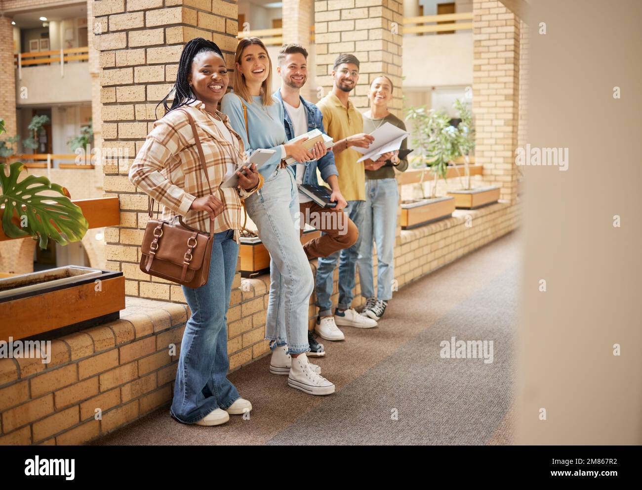 Universität, Lächeln und eine Gruppe von Schülern in der Lobby stehen in Reihe mit Büchern an der Wirtschaftsschule im Sommer. Freunde, Bildung und Vielfalt, Genz Stockfoto