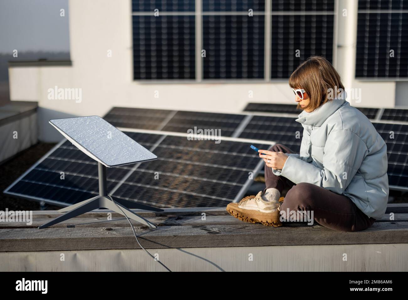 Frau benutzt Starlink Internet auf dem Dach mit Solarpaneelen Stockfoto