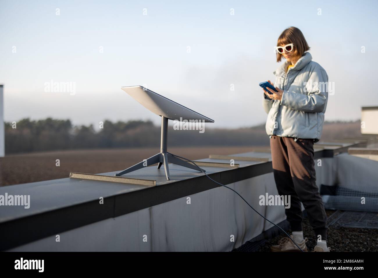 Eine Frau mit Telefon benutzt Starlink-Satelliten-Internet auf dem Dach Stockfoto