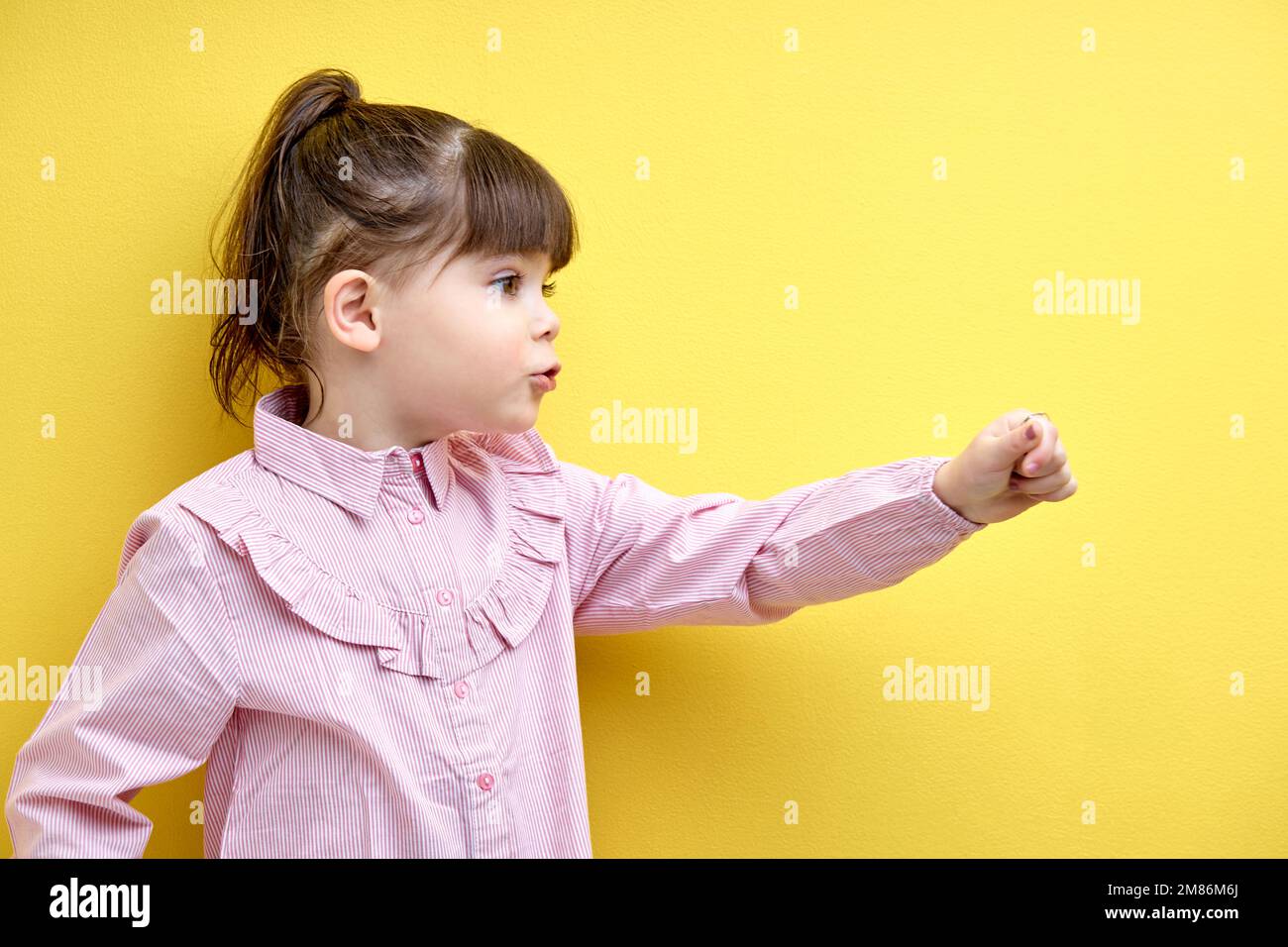Seitliches Porträt eines Kindes, das zur Seite schaut und spricht, zeigt Hand nach vorne, lustiges und emotionales Kind mit Pferdeschwanz isoliert auf gelbem Hintergrund Stockfoto