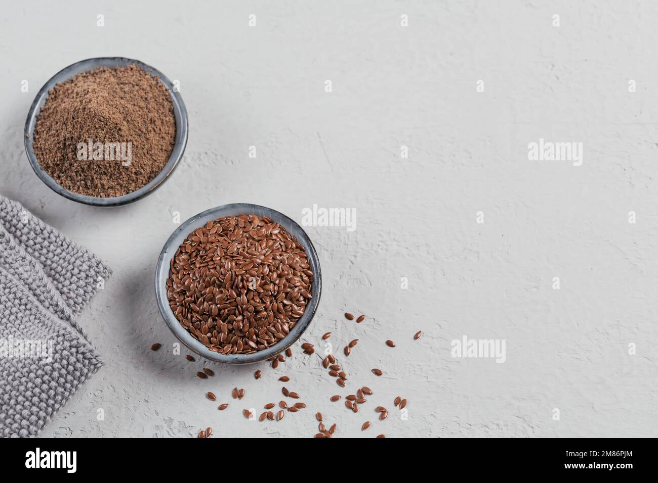 Braune Leinsamen und gemahlene oder zerkleinerte Leinsamen oder Leinsamen in einer kleinen Schüssel auf hellgrauem Hintergrund. Stockfoto