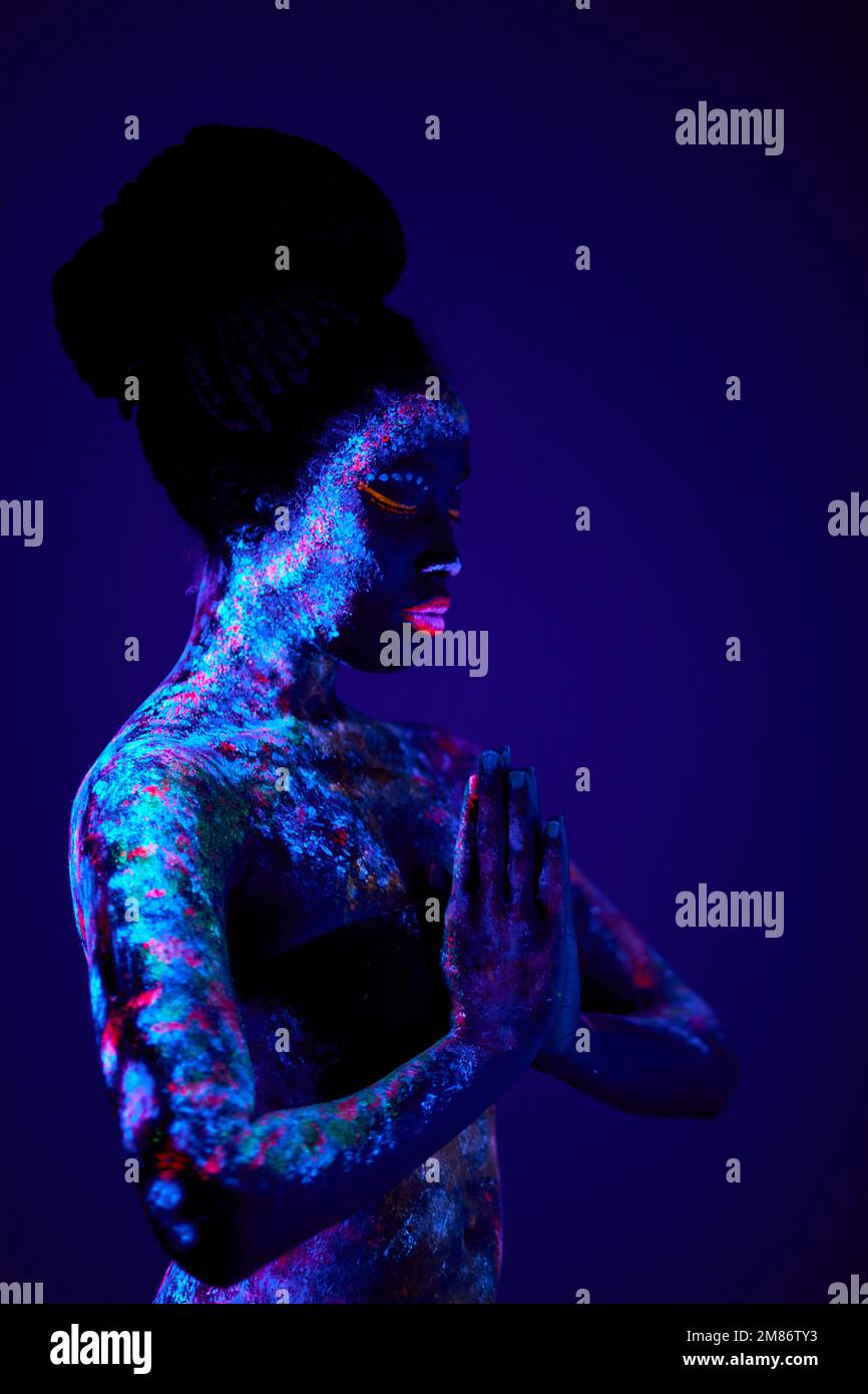 Junge schlanke schwarze Gebetsfrau mit bunten fluoreszierenden Drucken auf der Haut, schöne weibliche beten, bitten um Segen. Drucke leuchtet in UV-Licht. Körperkunst, Stockfoto