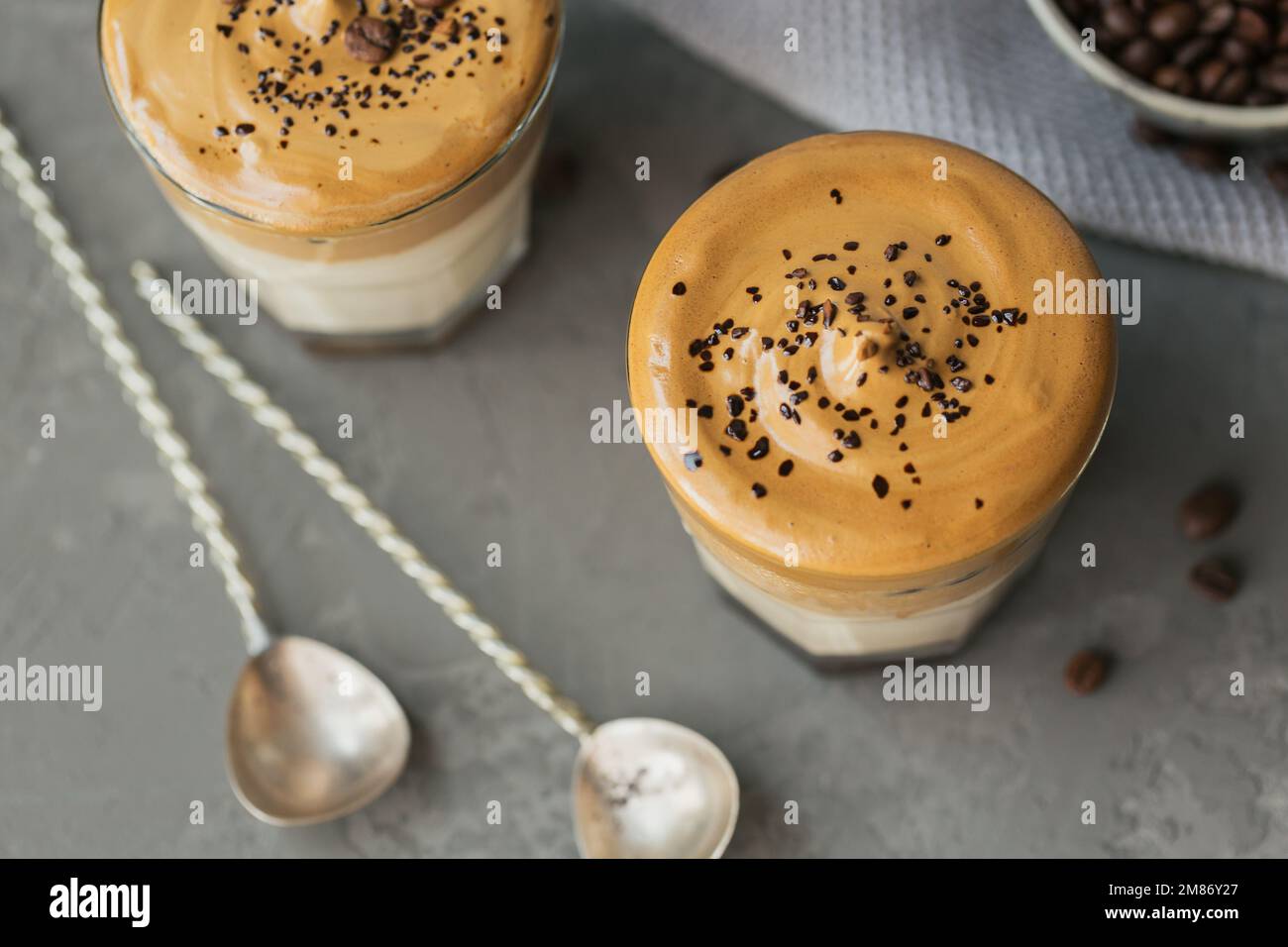 Ein Glas Iced Dalgona Kaffee, trendiger, flauschiger, cremiger Schlagsahne Kaffee und Milch auf grauem Hintergrund. Stockfoto