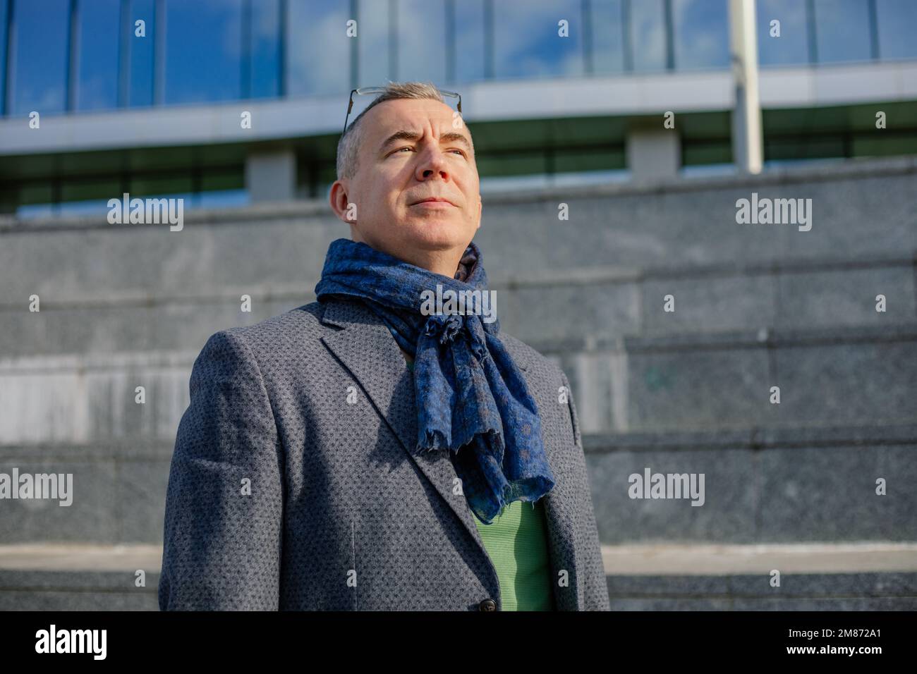 Selbstbewusster, moderner, reifer, grauhaariger Geschäftsmann mit Brillen in Jacke und Schal, Fußgängerzone in der Nähe des Bürogebäudes. Stockfoto