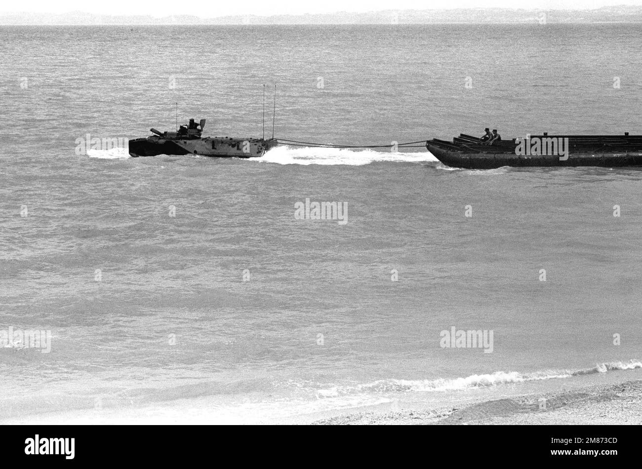 Ein AAV-7-Amphibienfahrzeug der Kompanie A, 2. Assault Amphibian Bataillon, schleppt einen Abschnitt der Brücke hinaus ins Meer, wo es mit anderen Abschnitten verbunden wird, um während einer Überbrückungsübung vor Kin Blue Beach eine Fähre zu bilden. Marines von Co B, 9. Engineer Support BN., 3. Force Service Support GRP., nehmen ebenfalls an der Übung Teil. Staat: Okinawa Land: Japan (JPN) Stockfoto