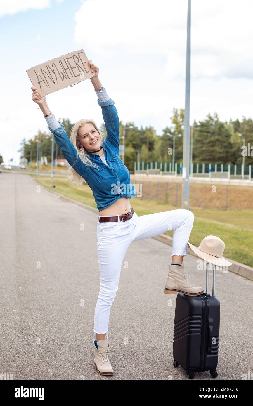 Eine aufrechte, positiv lachende, blonde Frau, die automatisch stoppt, überall Pappteller hält, mit erhobenem Bein auf dem Gepäck Stockfoto