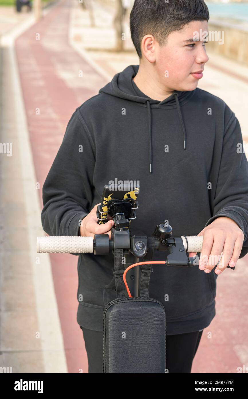 Junger Teenager mit einem seitlichen Blick, der auf einem elektrischen Skateboard fährt und eine Smartphone-Anwendung verwendet Stockfoto