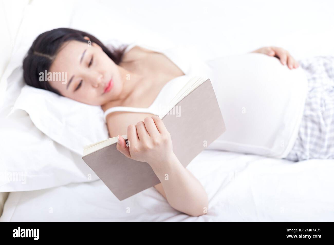 Schwangere Frau, die im Bett liegt und ein Buch liest Stockfoto