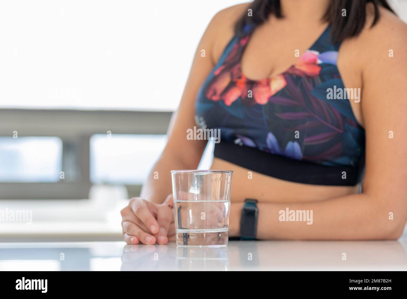 Nahaufnahme der Hände einer Frau, die ein Glas Wasser hielt, auf einer Küchentheke in einem Sportstudio. Stockfoto