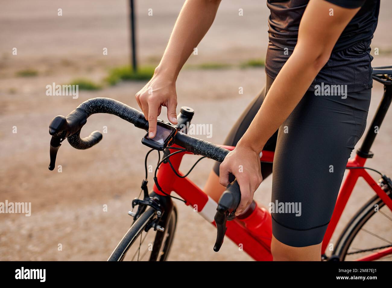 Sportlicher junger Mann mit starken Beinen, der auf der Straße mit rotem Fahrrad steht. Sonnenuntergang, Abendzeit. Radfahrkonzept. Ein verkürzter, nicht wiedererkennbarer Typ in sportlichen Outfits Stockfoto