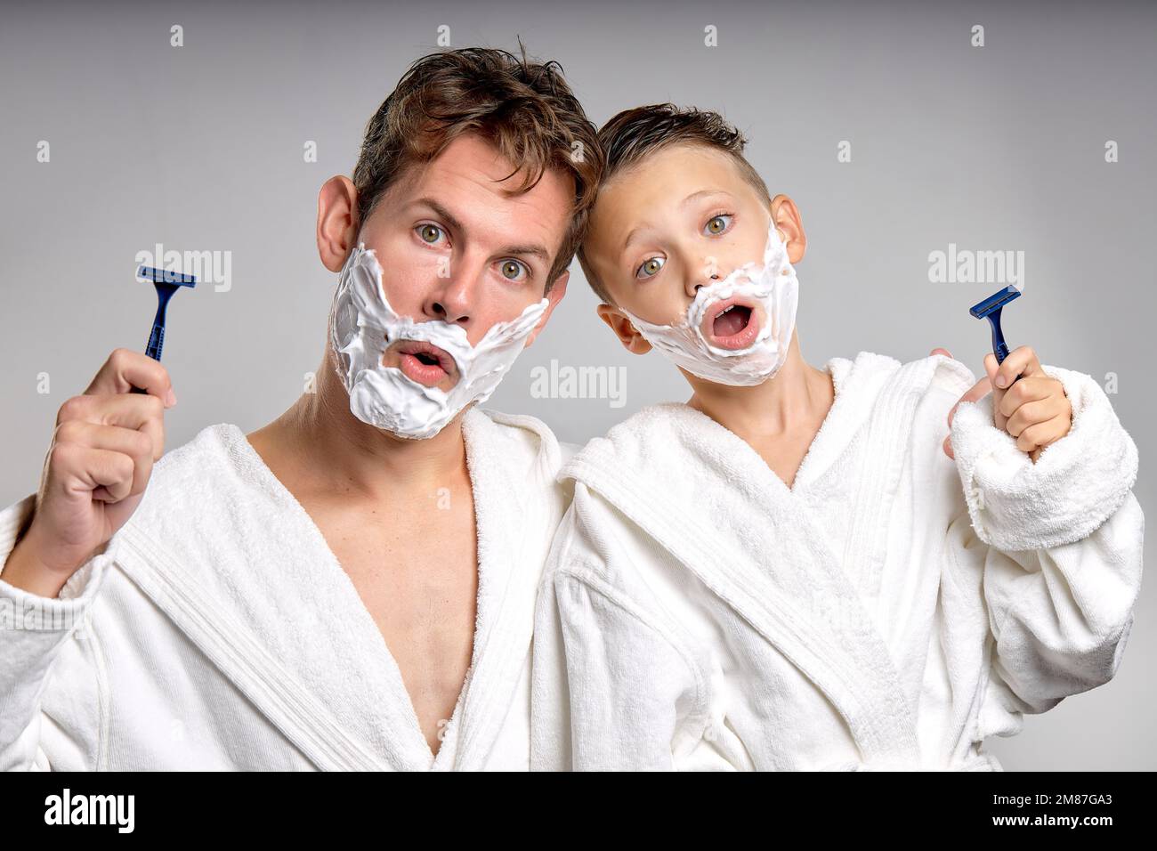männlicher weißer und kleiner Junge, die Spaß mit Rasierschaum auf den Gesichtern im Bad haben, isoliert. Lustig Happy Vater und Sohn rasieren Gesichter am Morgen Stockfoto