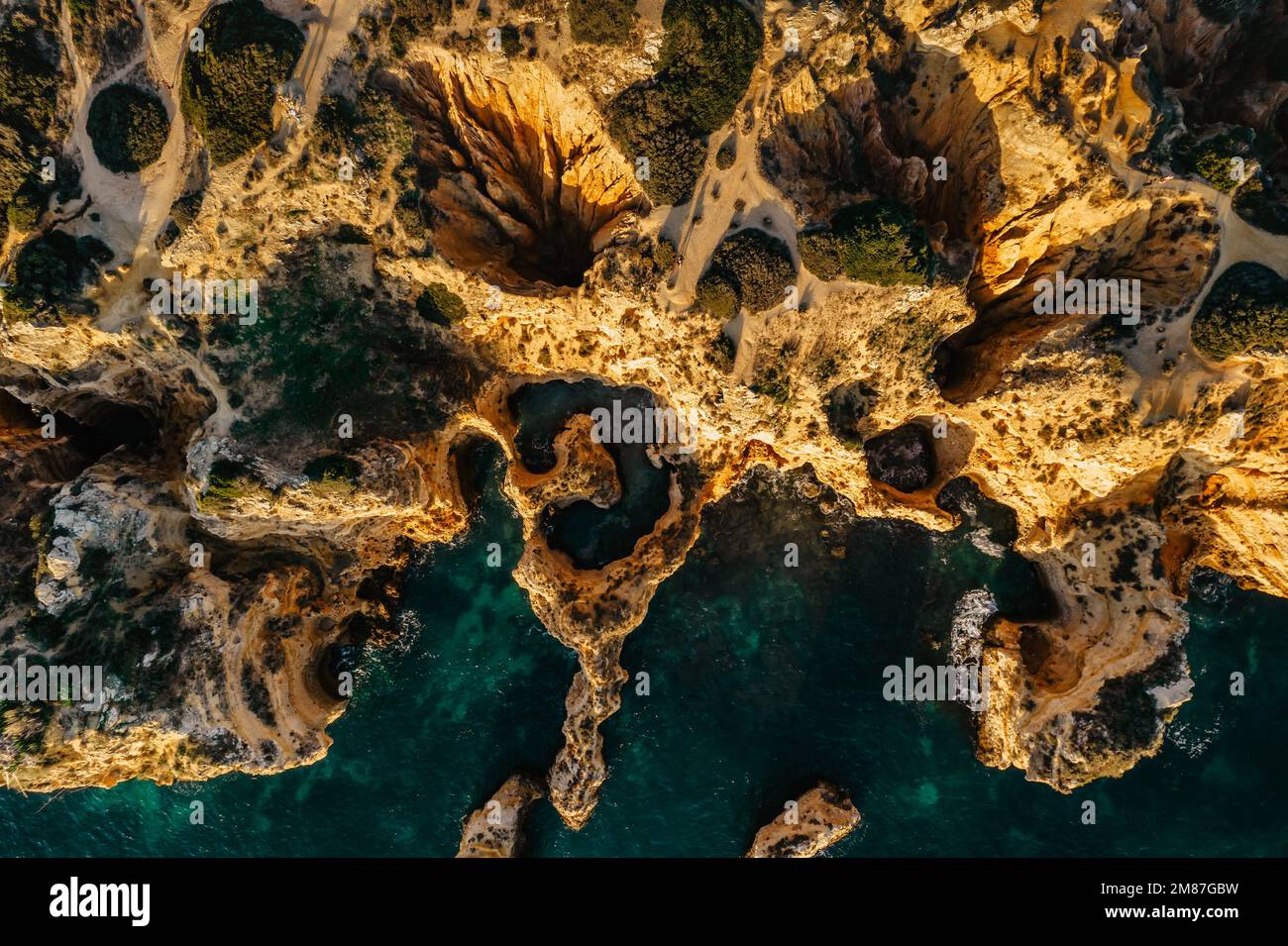 Blick aus der Vogelperspektive auf die goldenen Klippen der Küste bei Sonnenaufgang in Ponta da Piedade in der Nähe von Lagos, Portugal. Spektakuläre Felsformationen mit Höhlen, Löchern und Meeresbögen. Stockfoto
