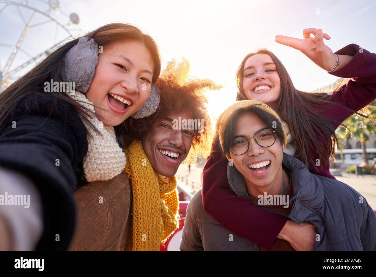 Ein glückliches Selfie mit einer Gruppe von vier internationalen Freunden, die im Winter Huckepack draußen in der Stadt machen. Stockfoto