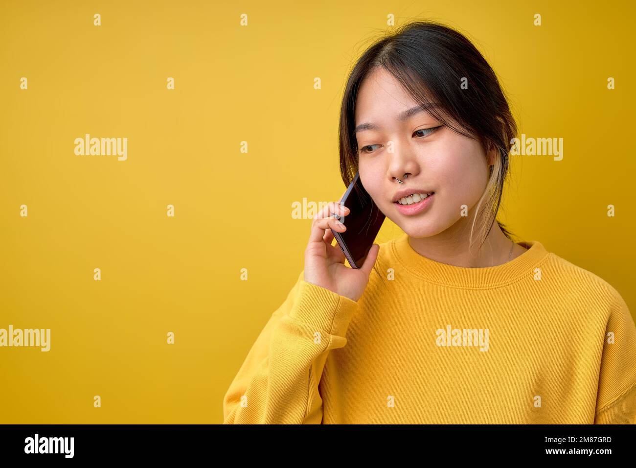 Wunderschöne junge asiatische Frau, die isoliert auf gelbem Hintergrund steht und ein Smartphone hält, das mit jemandem am Telefon spricht. Bereich Kopieren. Moderne Chinesin Stockfoto