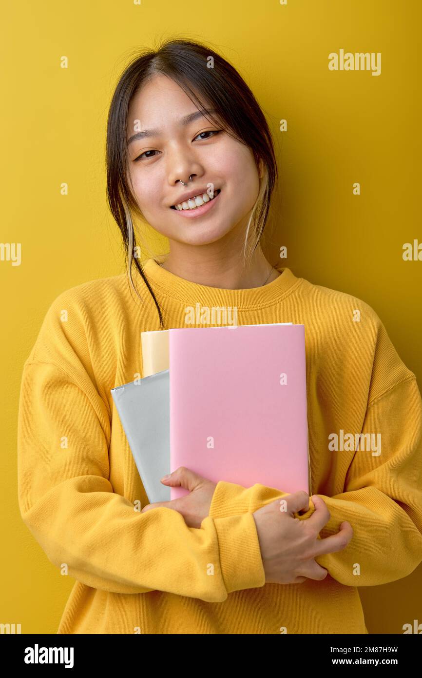 Angenehm fröhlich attraktiv schöne junge brünette asiatische Frau 20s mit legerem gelbem Hemd und Büchern isoliert auf hellgelb Stockfoto