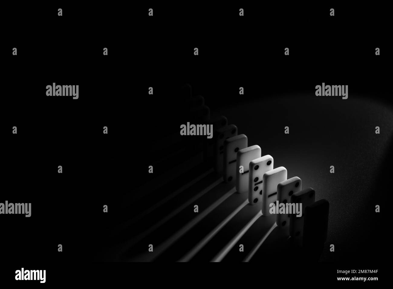Dominosteine auf einem Tisch im Dunkeln mit einem Lichtstrahl, Schwarz-Weiß-Foto, spielen Dominosteine Nahaufnahme Stockfoto