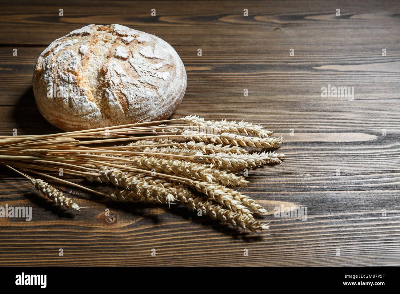 Frisch gebackener Brotbraten und Weizenohren auf Holzhintergrund. Lebensmittelversorgung und Produktionskonzept. Stockfoto