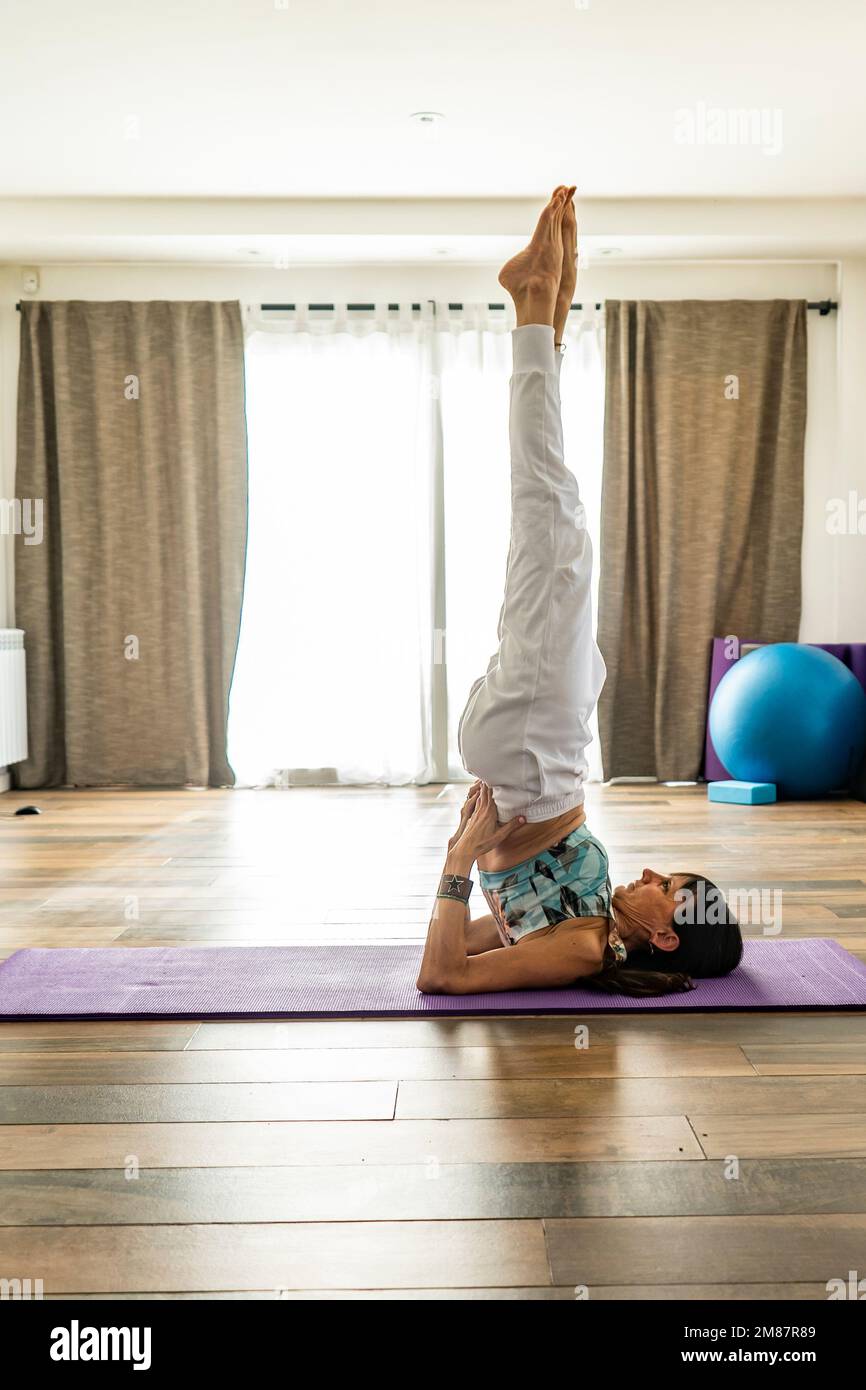 Seitenansicht einer Frau, die Yoga praktiziert, die am Schulterständer posiert. Yoga-Studio Stockfoto