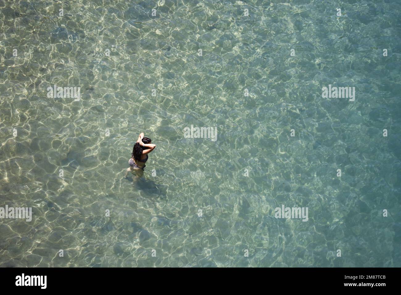 Luftaufnahme zum azurblauen Meer und Frau, die im transparenten Wasser schwimmen geht. Sonnige Ferien, Strandurlaub Stockfoto