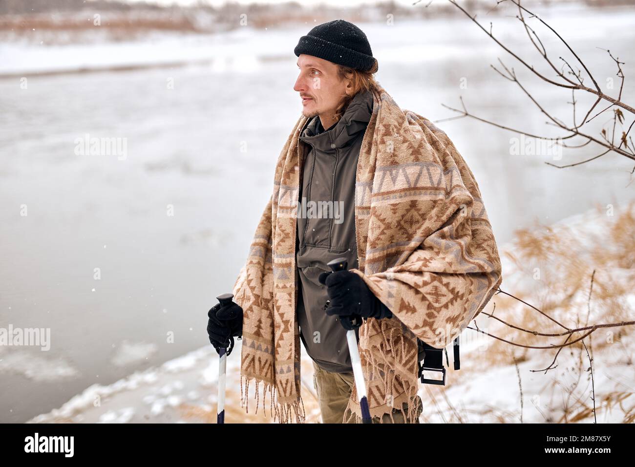 Porträt eines aktiven Mannes mittleren Alters, der im Winterschneewald wandert. Attraktiver Kerl mit Mantel, Schal und Hut, der zur Seite schaut und sich ausruht. Wintermonat Stockfoto
