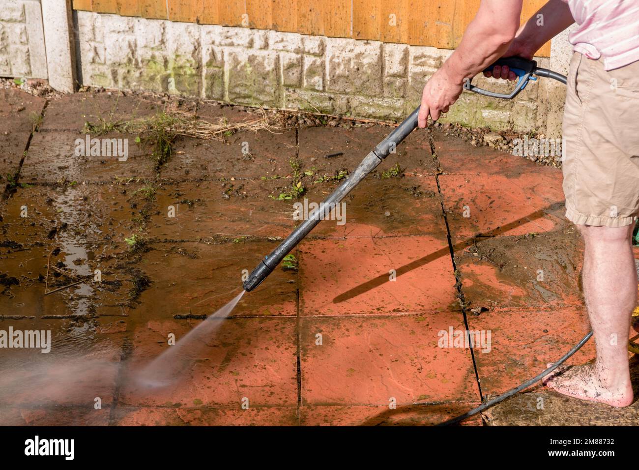 Ein Mann, der einen Hochdruckreiniger benutzt, um eine schmutzige, verschmutzte Terrasse mit einem Druckwasserstrahl zu reinigen Stockfoto