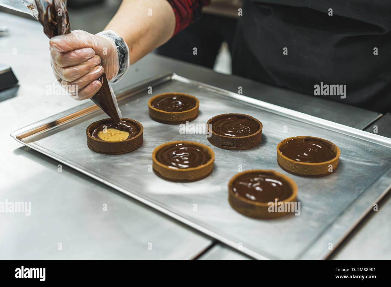 Der Koch fügte geschmolzene Schokolade in einem Paspelbeutel zu den gebackenen Plätzchen auf einem Tablett hinzu, Backvorgang. Hochwertiges Foto Stockfoto
