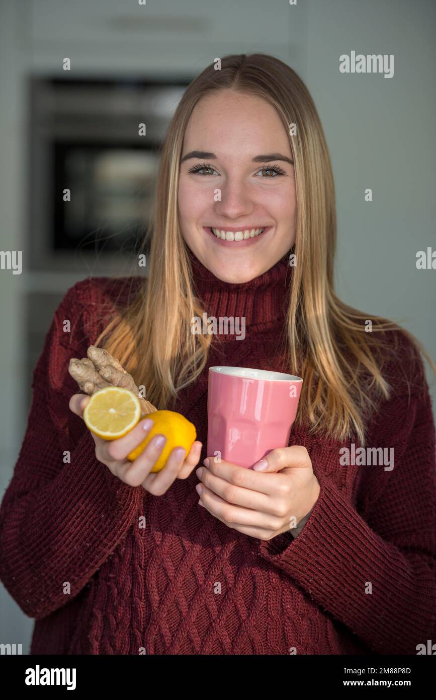 Junge Frau, in der Küche, mit Ingwer, Zitrone und Teetasse, Hausmittel, Kaltes Oberbayern, Bayern, Deutschland, Europa Stockfoto