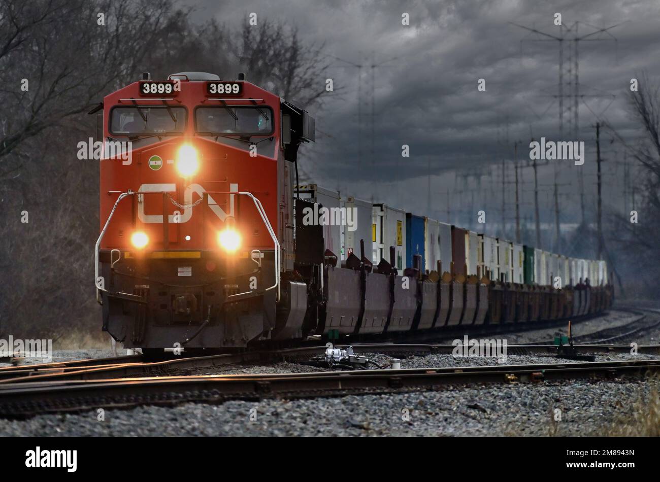Elgin, Illinois, USA. Mit einem Labyrinth aus Stromleitungen und Türmen im Hintergrund treibt eine Lokomotive der Canadian National Railway eine intermodale Fracht an. Stockfoto