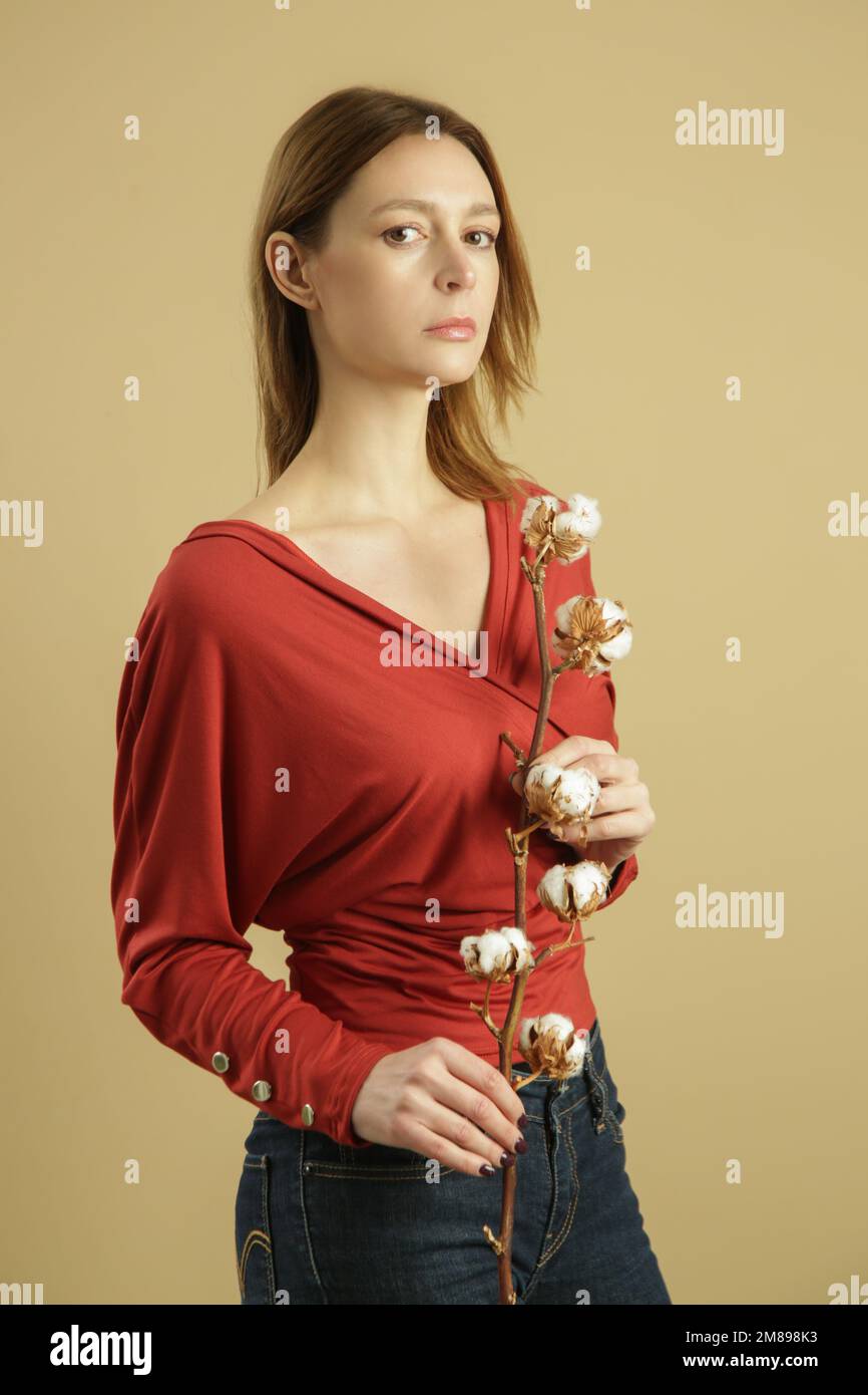 Studiofoto eines jungen weiblichen Models im Hemd aus biologischer Baumwolle mit Baumwollblumen. Konzept von komfortabler und nachhaltiger Mode. Stockfoto
