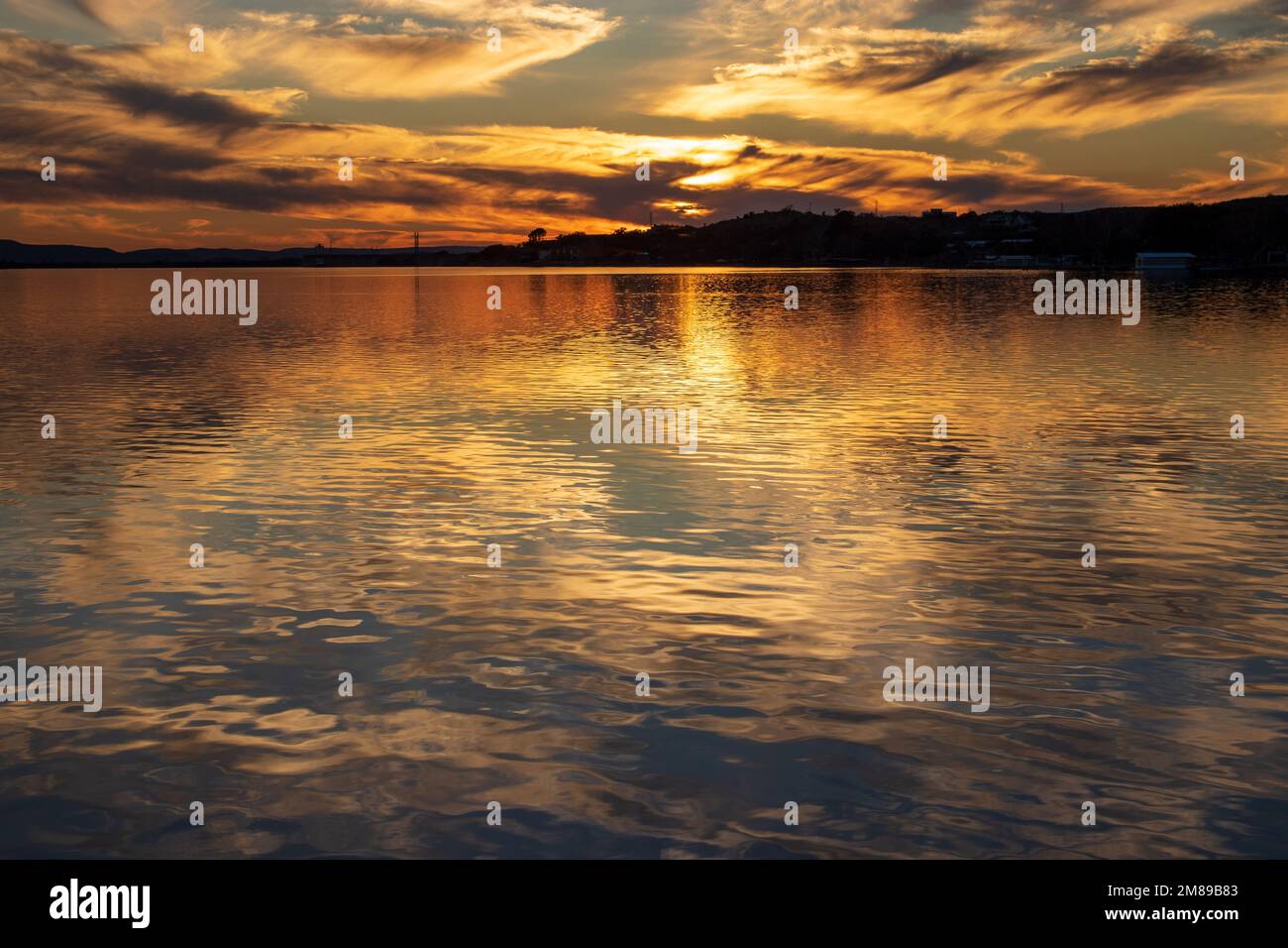 Sonnenuntergang über dem Inks Lake im Inks Lake State Park Texas USA. Der Himmel leuchtet, wenn die Reflexionen der Wolken schimmern und das goldene Licht Schatten wirft. Stockfoto