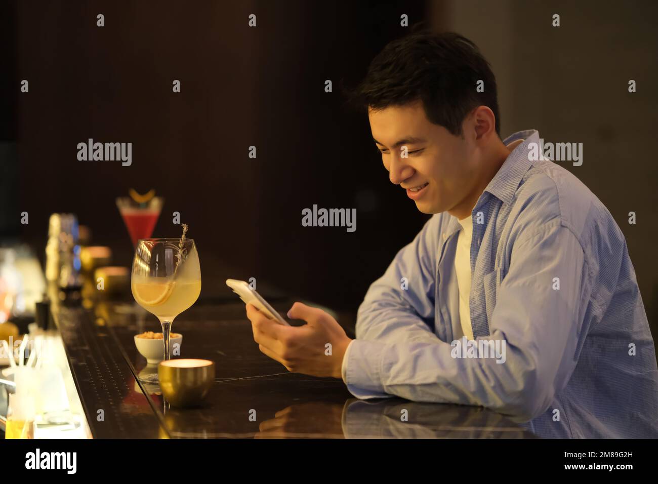 Ein hübscher junger chinesischer Mann schaut auf das Telefon an der Nachtbar Stockfoto