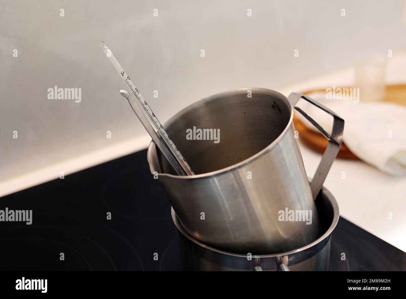 Erhitzen Sie die Messkanne mit Wasser und Jojobaöl in kochendem Wasser, und zeichnen Sie die Temperatur mit einem Thermometer auf Stockfoto
