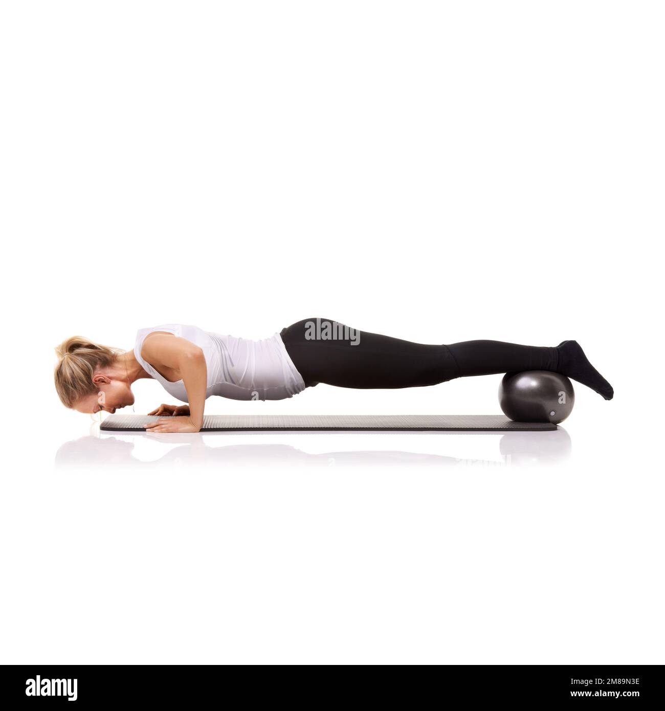 Das Streben nach Fitness lohnt sich auf jeden Fall. Eine junge Frau, die Push-Ups macht, während sie mit einem Sportball ihre Beine hebt. Stockfoto