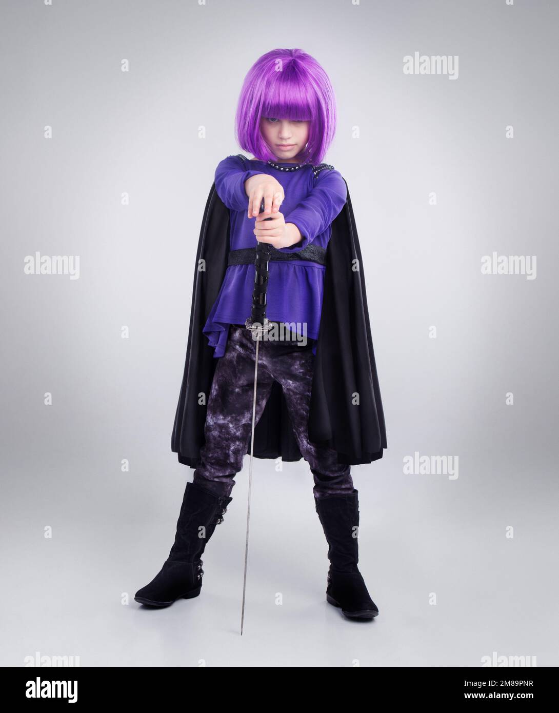 Kleines Mädchen, Superheld und halloween verkleiden sich mit Schwert vor grauem Studiohintergrund. Porträt eines Mädchens, das mit einem Superhelden spielt Stockfoto