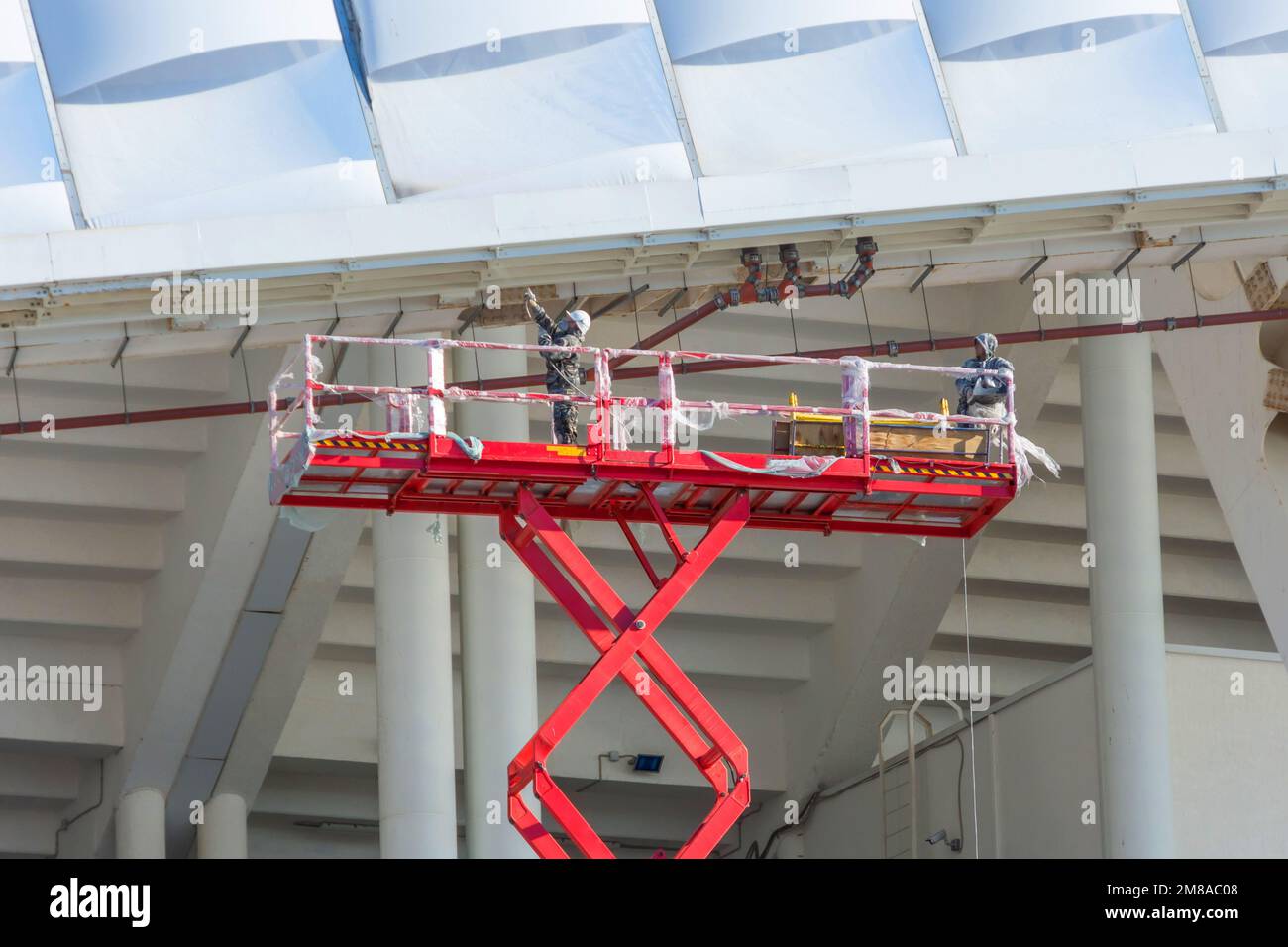 Bauarbeiter stehen in der Schere und heben Kranschaufel an, während sie auf hoher Höhe auf der Baustelle arbeiten Stockfoto
