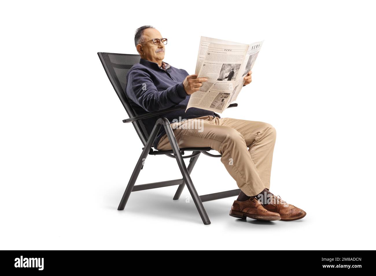 Zwangloser reifer Mann, der auf einem Klappstuhl sitzt und eine Zeitung liest, isoliert auf weißem Hintergrund Stockfoto